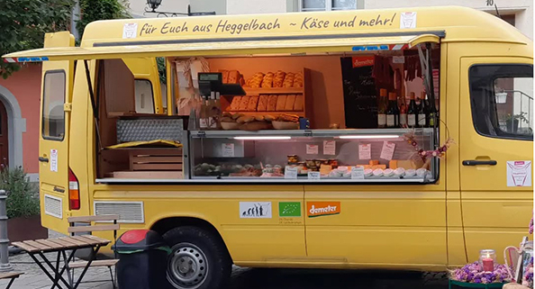 Besucher schlendern über den Konstanzer Bio-Markt auf der Konzil-Mole: Stände mit Käse, Brotaufstrichen, Gemüse und Wein von regionalen Erzeugern, darunter die Hofkäserei Heggelbach und Delikat essen.