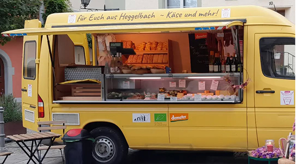 GvS_Hofgemeinschaft_heggelbach Besucher schlendern über den Konstanzer Bio-Markt auf der Konzil-Mole: Stände mit Käse, Brotaufstrichen, Gemüse und Wein von regionalen Erzeugern, darunter die Hofkäserei Heggelbach und Delikat essen.